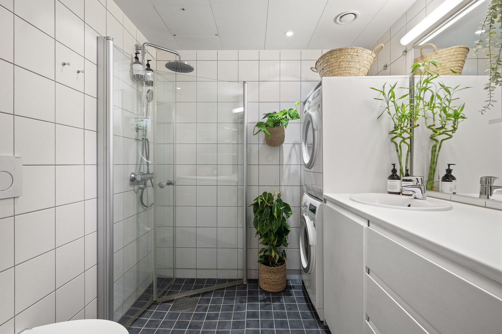 Innbydende og meget romslig bad med hvite fliser på vegg, gråmelerte fliser med varme i gulv og downlights i himling Galleribilde