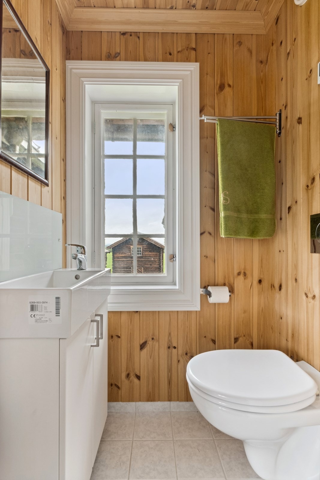 Toalettrom i 2. etasje med panel på vegger og i himling, og lyse spraglete fliser på gulvet. Toalettrommet er innredet med servant i hvit skapinnredning og veggmontert toalett. Galleribilde