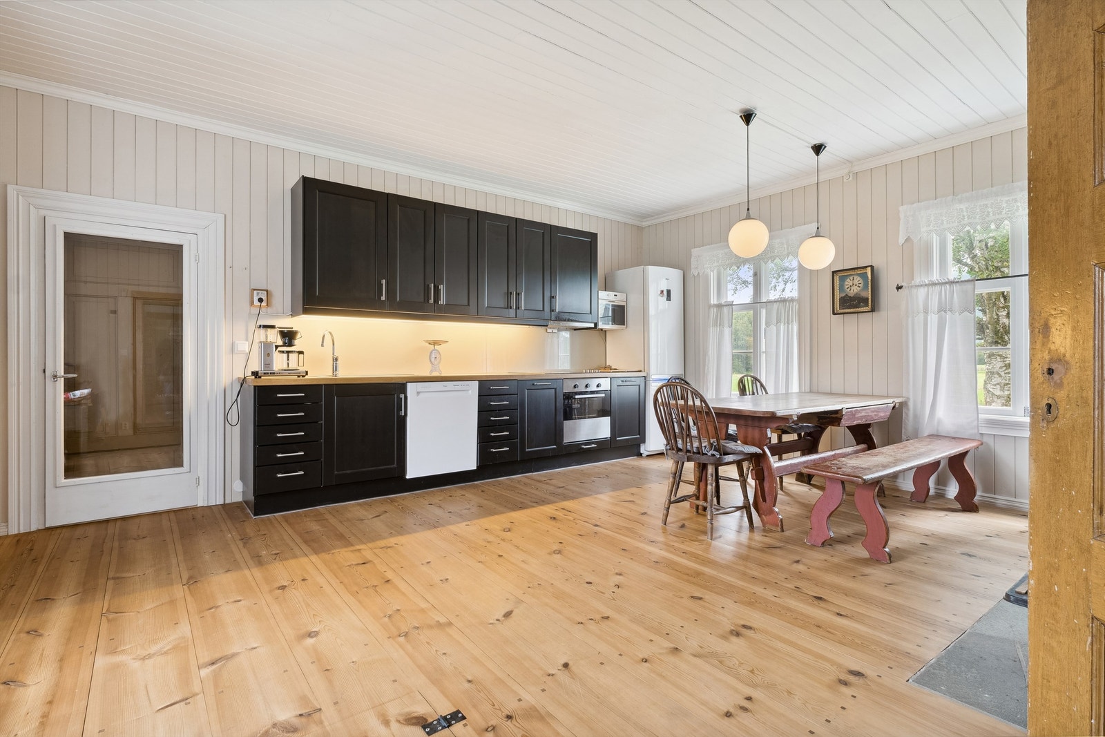 Kjøkkenet har lysmalt panel på veggene, hvitmalt panel i himling og furugulv. Mørk kjøkkeninnredning med profilerte fronter og heltre benkeplater. Galleribilde