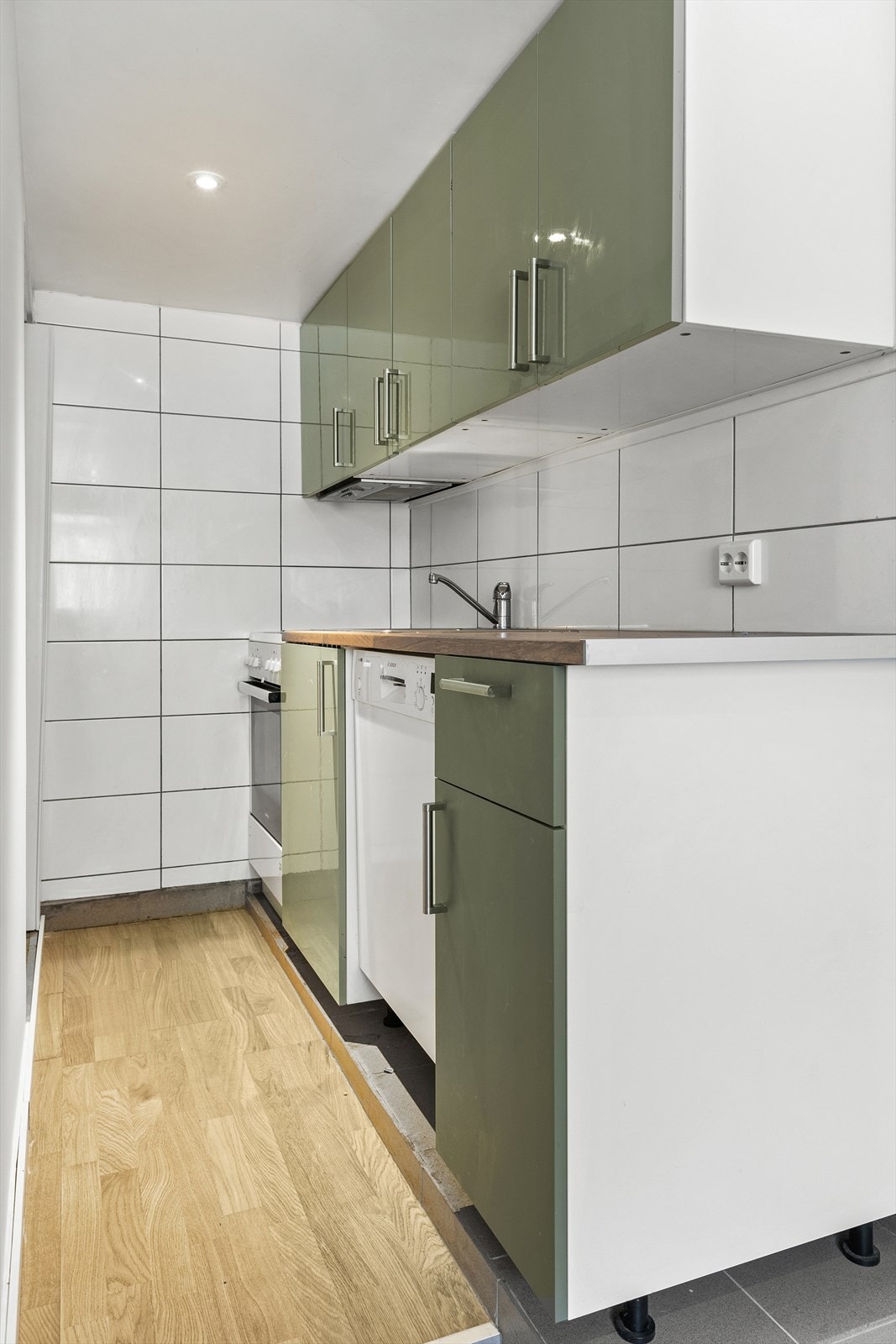 Enkel kjøkkeninnredning i kjeller med fliser over laminat benkeplate. Galleribilde