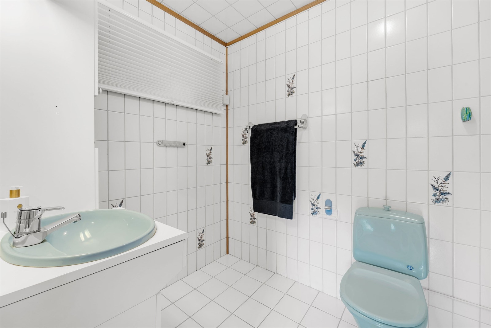 Begge badene har lyse fliser på gulv, vegger og i himling, samt lyseblått toalett og en servant i innredning. Galleribilde