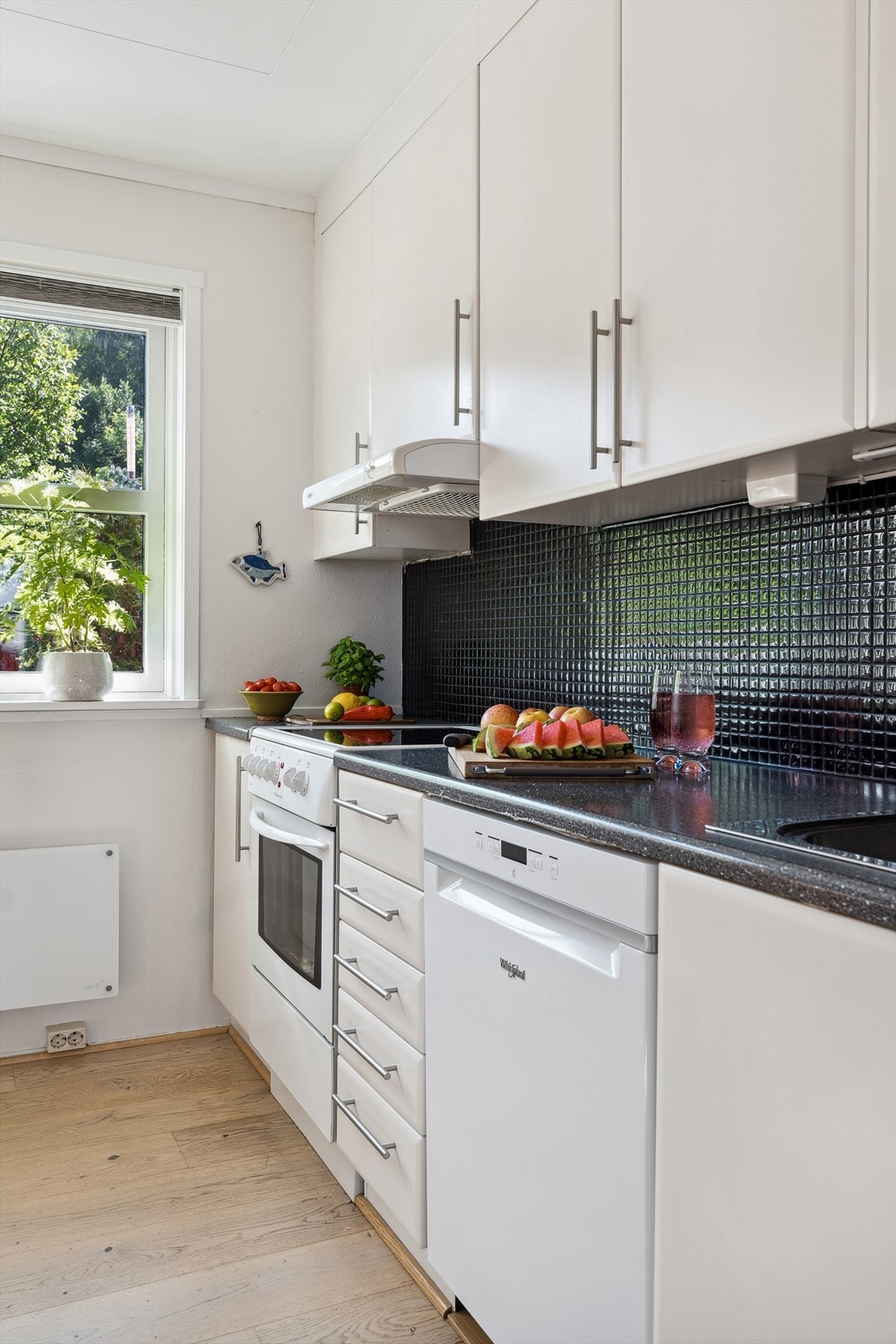 Moderne og tidløs kjøkkeninnredning med hvite glatte fronter og laminert benkeplate med nedfelt oppvaskkum. Praktisk med mørke fliser i benkeryggen og takhøye overskap med belysning under. Galleribilde