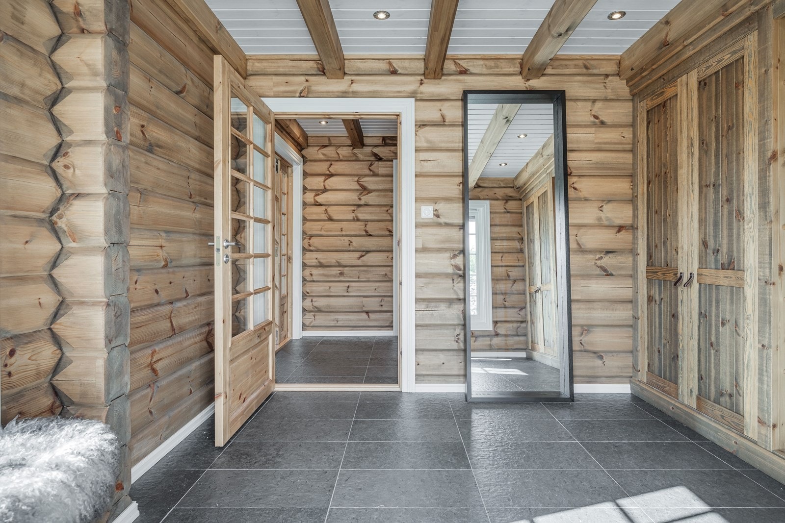 Hallen har mørke fliser på gulv med gulvvarme, vegger med laftet tømmer og downlights i himlingen. God plass til sko og yttertøy i flotte plassbygde garderobeskap. Galleribilde