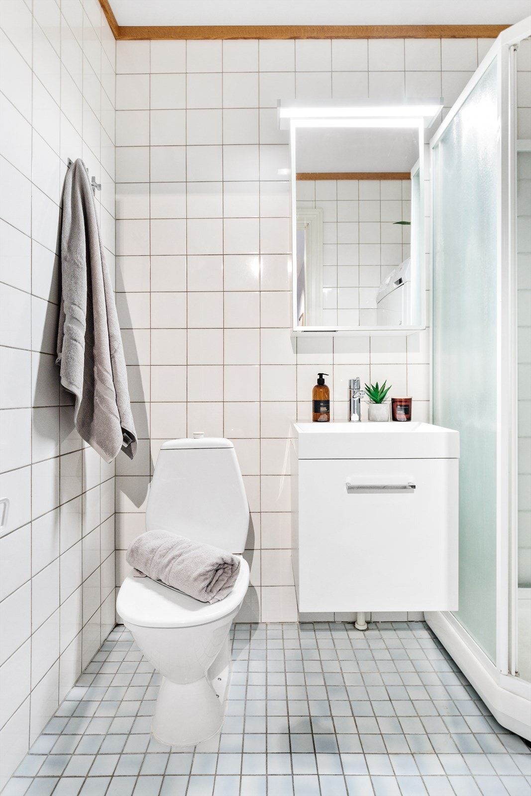 Flislagt bad med elektriske varmekabler i gulv, dusjkabinett, frittstående toalett og innredning med speilskap over vask. Galleribilde