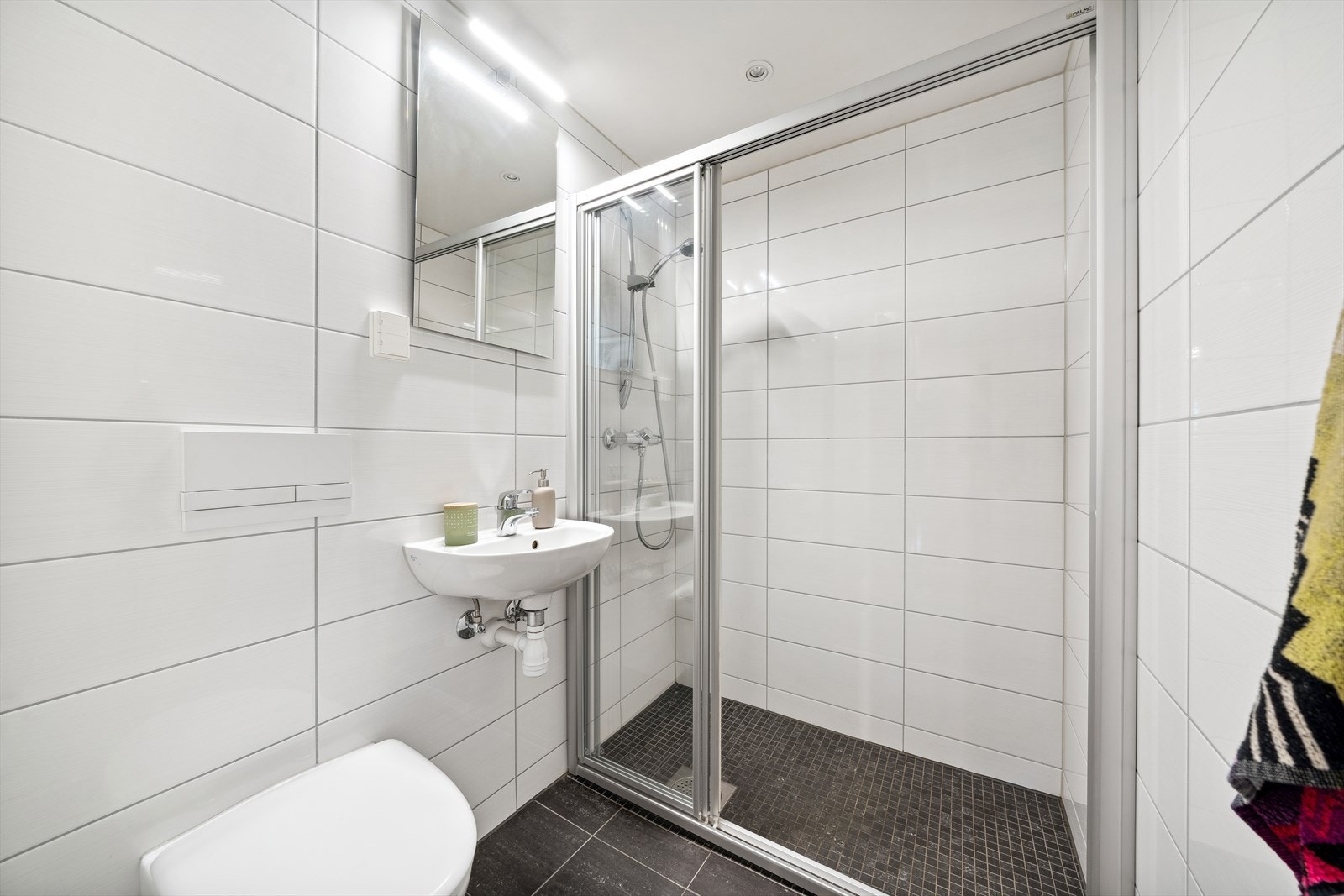 Bad 1 - Flislagt bad med flis på vegg og gulv, plater i taket. Badet er innredet med dusjvegg, servant og vegghengt toalett. Badet har downlights i taket og vannbåren gulvvarme Galleribilde