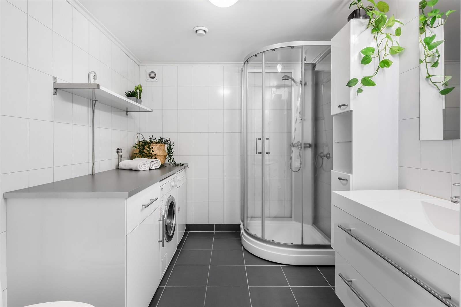 Lyst og pent bad, utstyrt med varmekabler, toalett og dusjkabinett, samt servantinnredning med heldekkende servant og opplegg for vaskemaskin og tørketrommel. Galleribilde