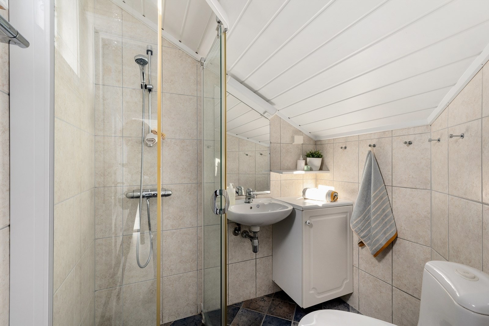 Dette badet ligger i andre etasje. Det er fliser, gulvvarme, praktisk innredning, toalett og et dusjhjørne. Galleribilde