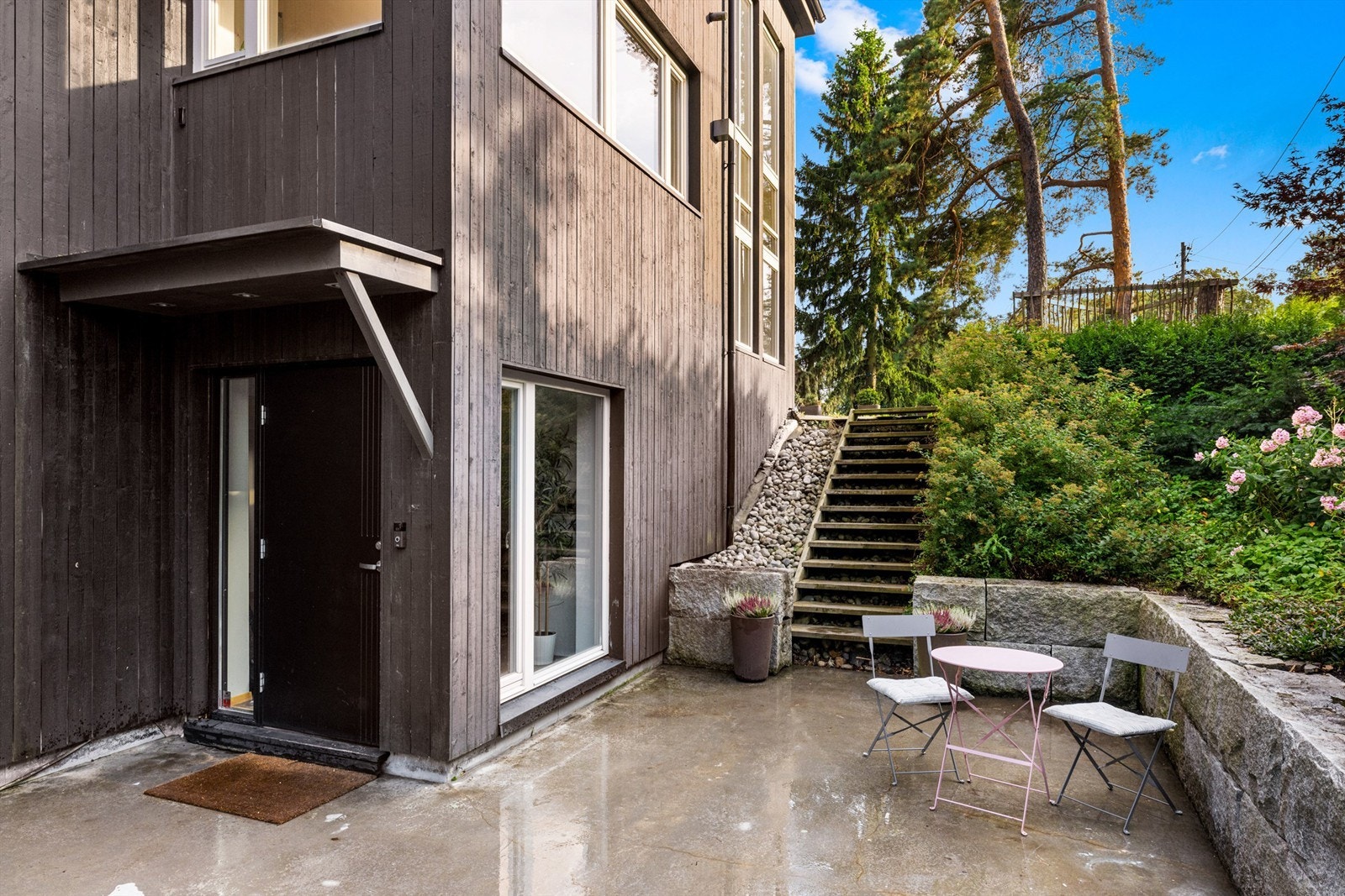 Tomt for boligen opparbeidet med busker, trær, utvendig bod, plenområder og oppkjørsel belagt med betong. Galleribilde