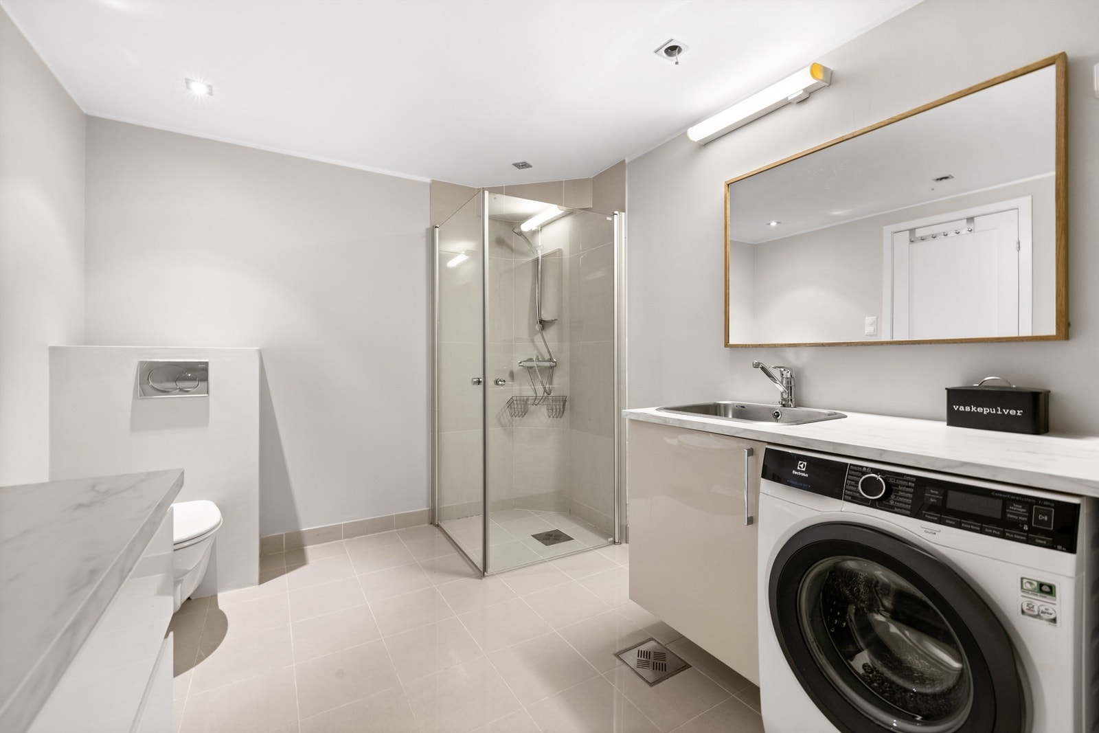 Bad/vaskerom fra byggeår. Dusjhjørne med innfellbare glassdører og to-greps armatur. Vegghengt toalett. Galleribilde