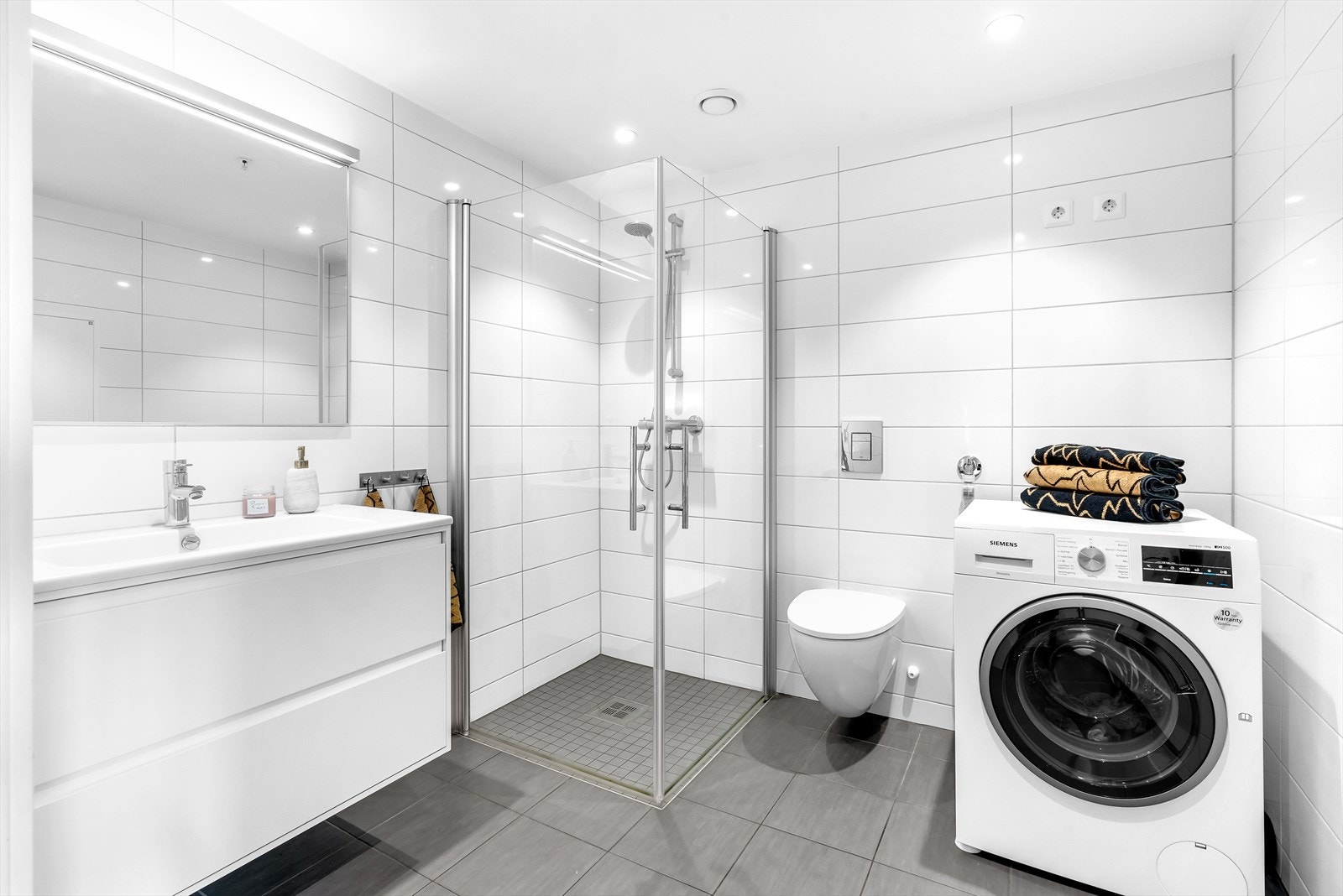 Pent flislagt baderom med vegghengt wc og opplegg for vaskemaskin. Varmekabler i gulv og downlights i himling. Galleribilde