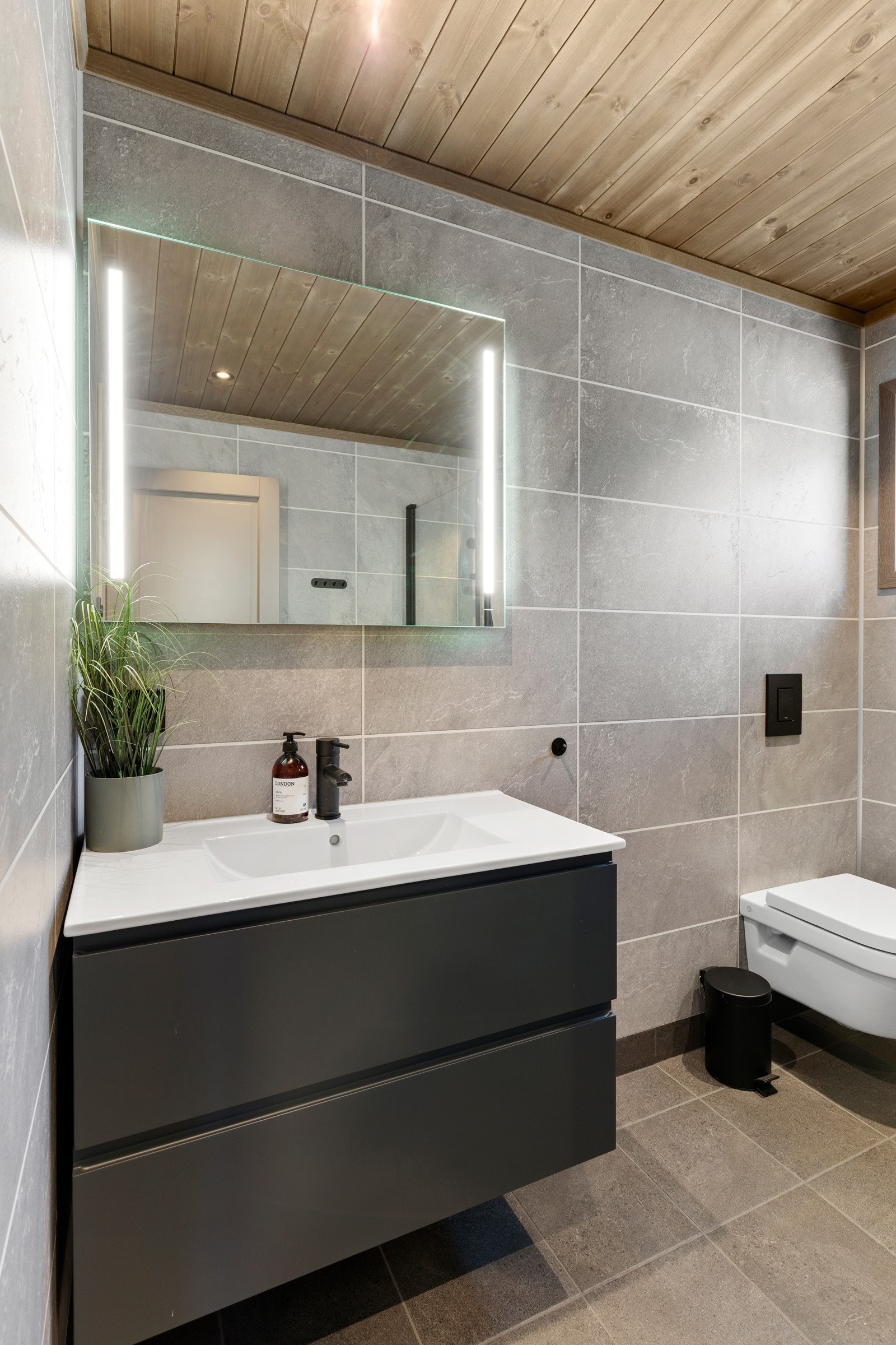 Badet er utstyrt med varmekabler i gulv, spotlights i himling, vegghengt toalett, dusj med glassdører, samt baderomsinnredning med servant og speil med belysning. Galleribilde