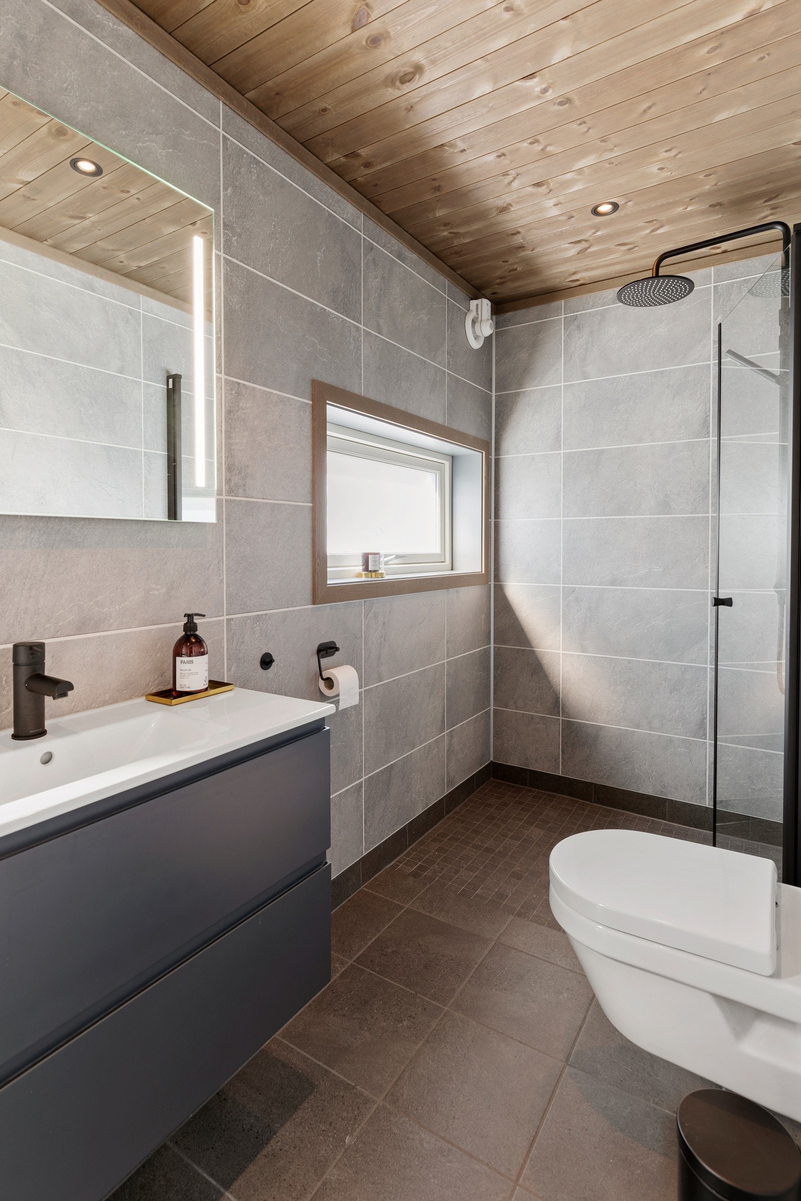 Videre inneholder badet spotlights i himling, vegghengt toalett, dusj med dusjvegger og baderomsinnredning med servant og speil med belysning. Galleribilde