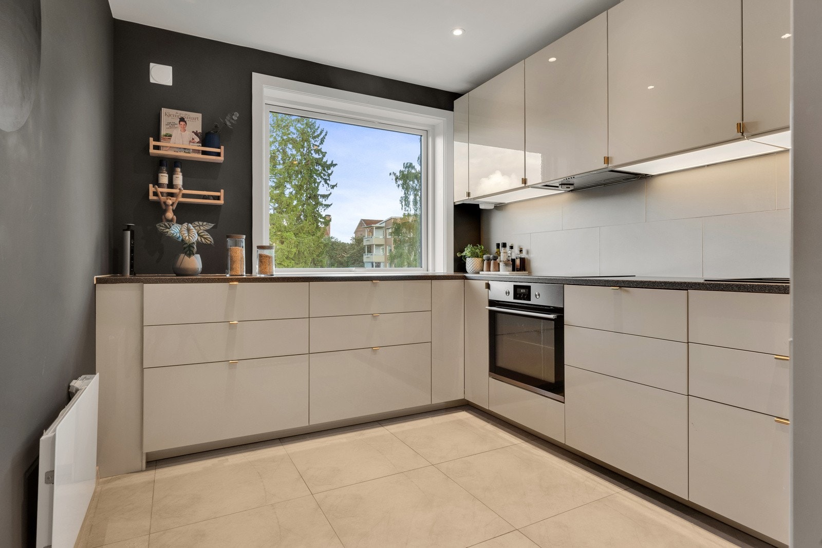 Kjøkkenet ligger i eget rom med store, sandfargede fliser på gulv, downlights i himling og plass til frokostbord Galleribilde