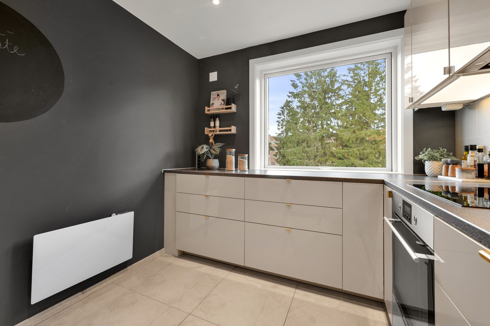 Innredningen er i et moderne design med beige, glatte fronter, benkeplate av laminat, oppvaskkum av kompositt og fliser på vegg over benk Galleribilde