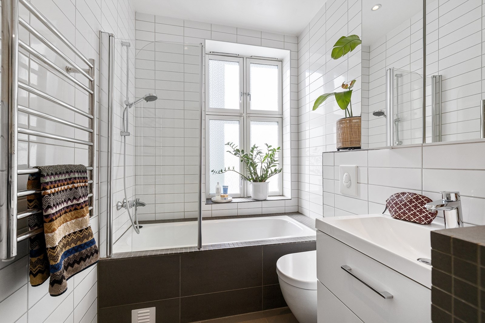 Videre er badet utstyrt med vegghengt toalett, innebygd badekar, servantinnredning med underskuffer, elektriske håndkletørker og opplegg for vaskemaskin Galleribilde