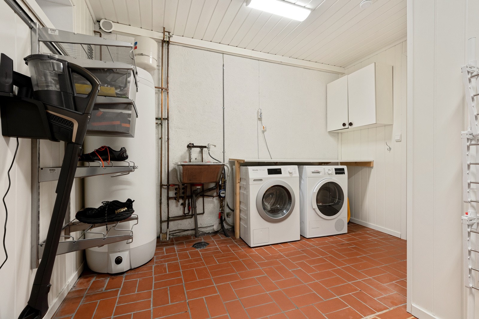 Vaskerom med eldre konstruksjon tilhørende hoveddel med skap, benkeplate, opplegg for vaskemaskin, og varmtvannsbereder fra 2019. Galleribilde