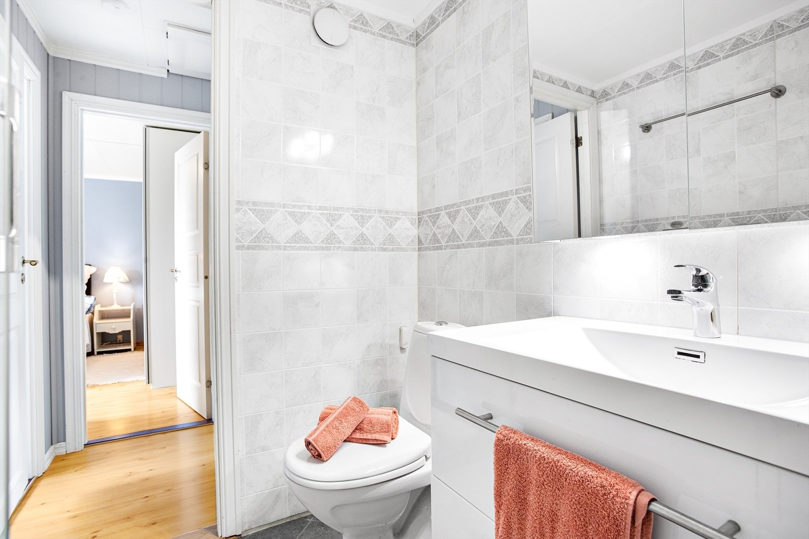 Badet har grå fliser på gulv med gulvvarme og lyse fliser med noe mønster på veggene. Galleribilde