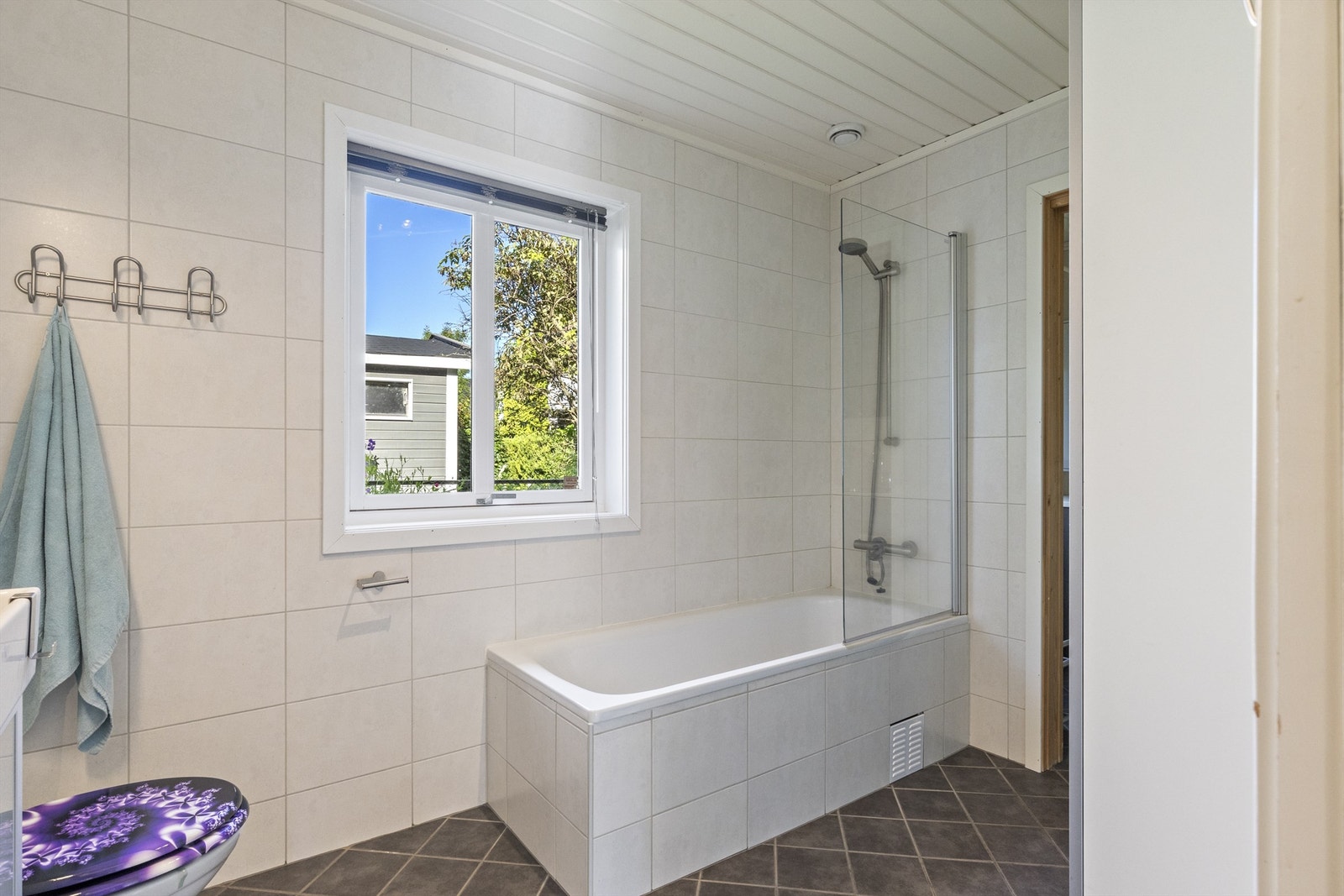 Badet har innfliset badekar med dusjvegg av glass og veggmontert hånddusj Galleribilde