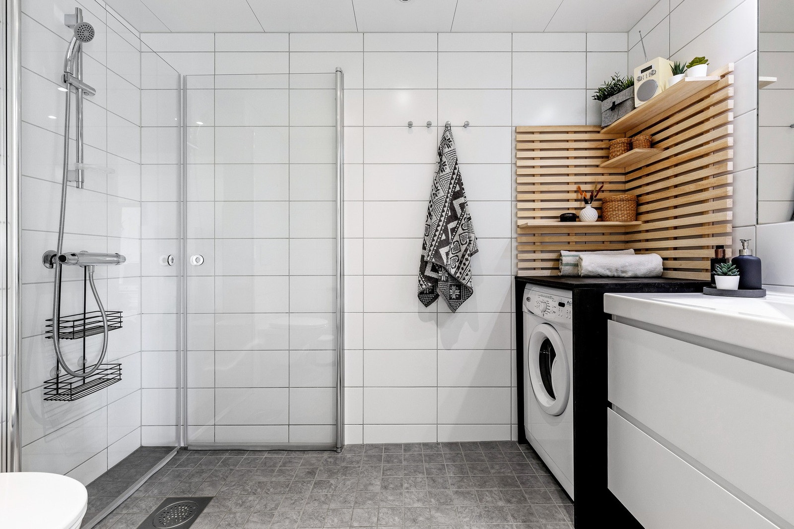 Lekkert flislagt bad med dusj, vegghengt wc, opplegg for vaskemaskin og servant i skap til oppbevaring. Galleribilde