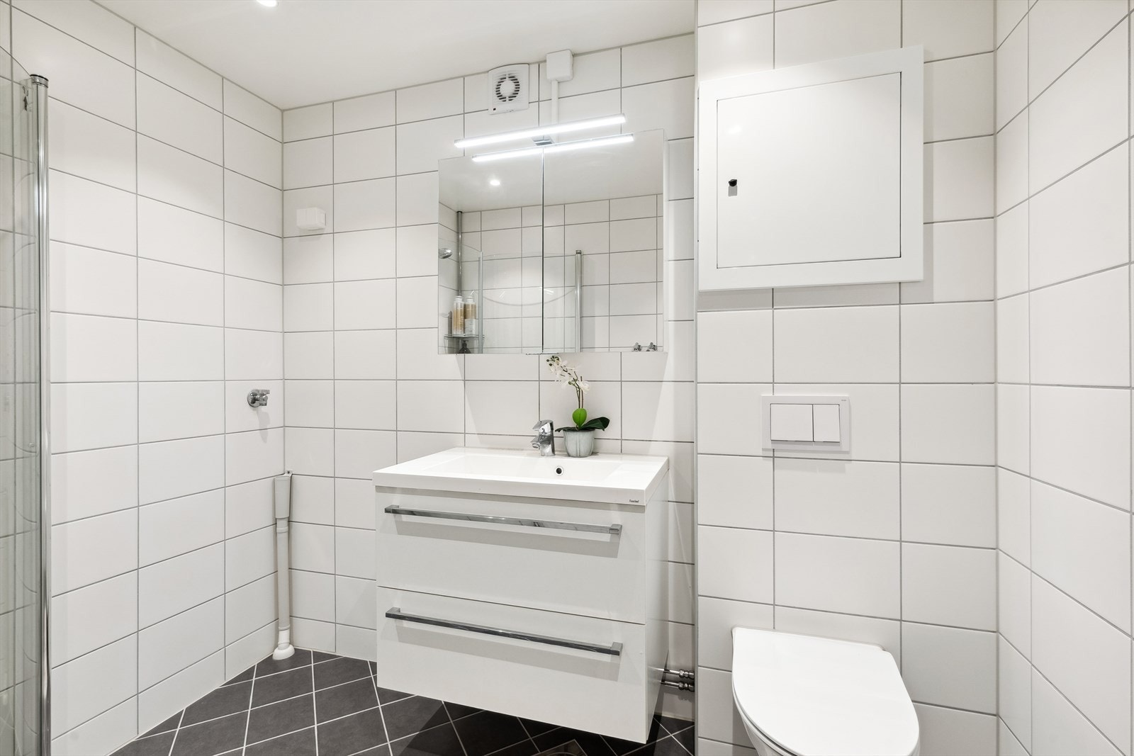 Badet er utstyrt med dusjhjørne med innfellbare glassvegger, vegghengt wc, servantinnredning med skuffer og overskap, samt opplegg og plass til både vaskemaskin og tørketrommel Galleribilde