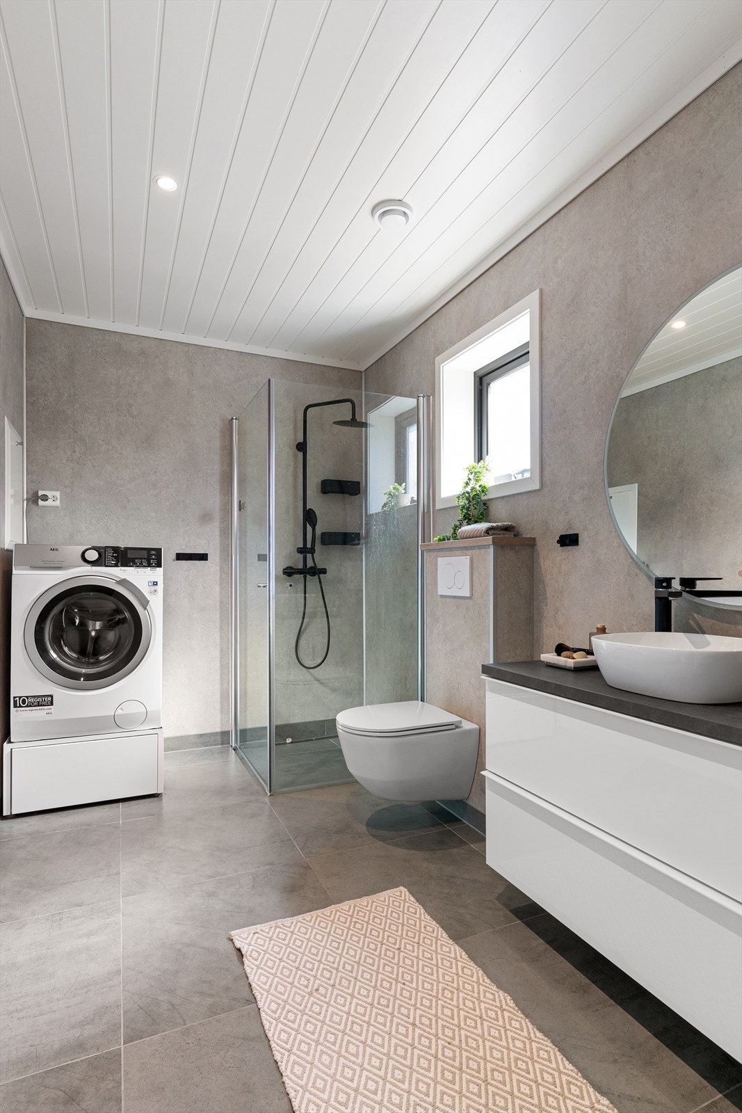 Badet inneholder innredning med toppmontert servant, speil med integrert lys, vegghengt toalett og dusjhjørne med glassdører. Det er også opplegg for vaskemaskin på badet. Galleribilde
