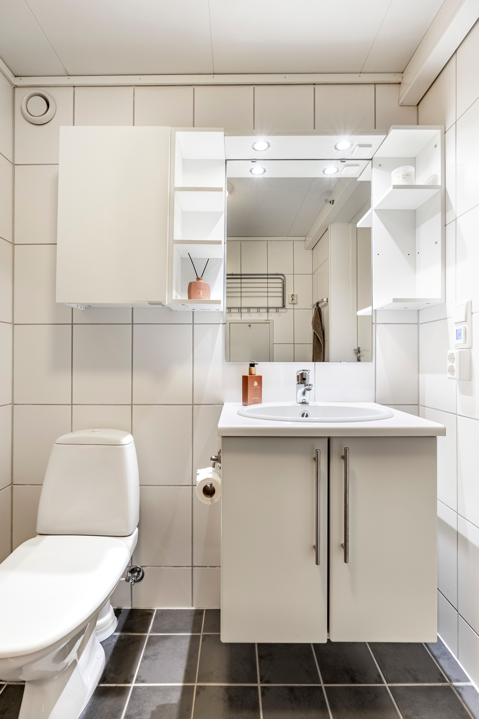 Badet er helfliset, har en fin størrelse og opplegg for vaskemaskin. Det er grå fliser på gulv med gulvvarme, hvite fliser på veggene, plafond i taket og mekanisk avtrekk. Galleribilde