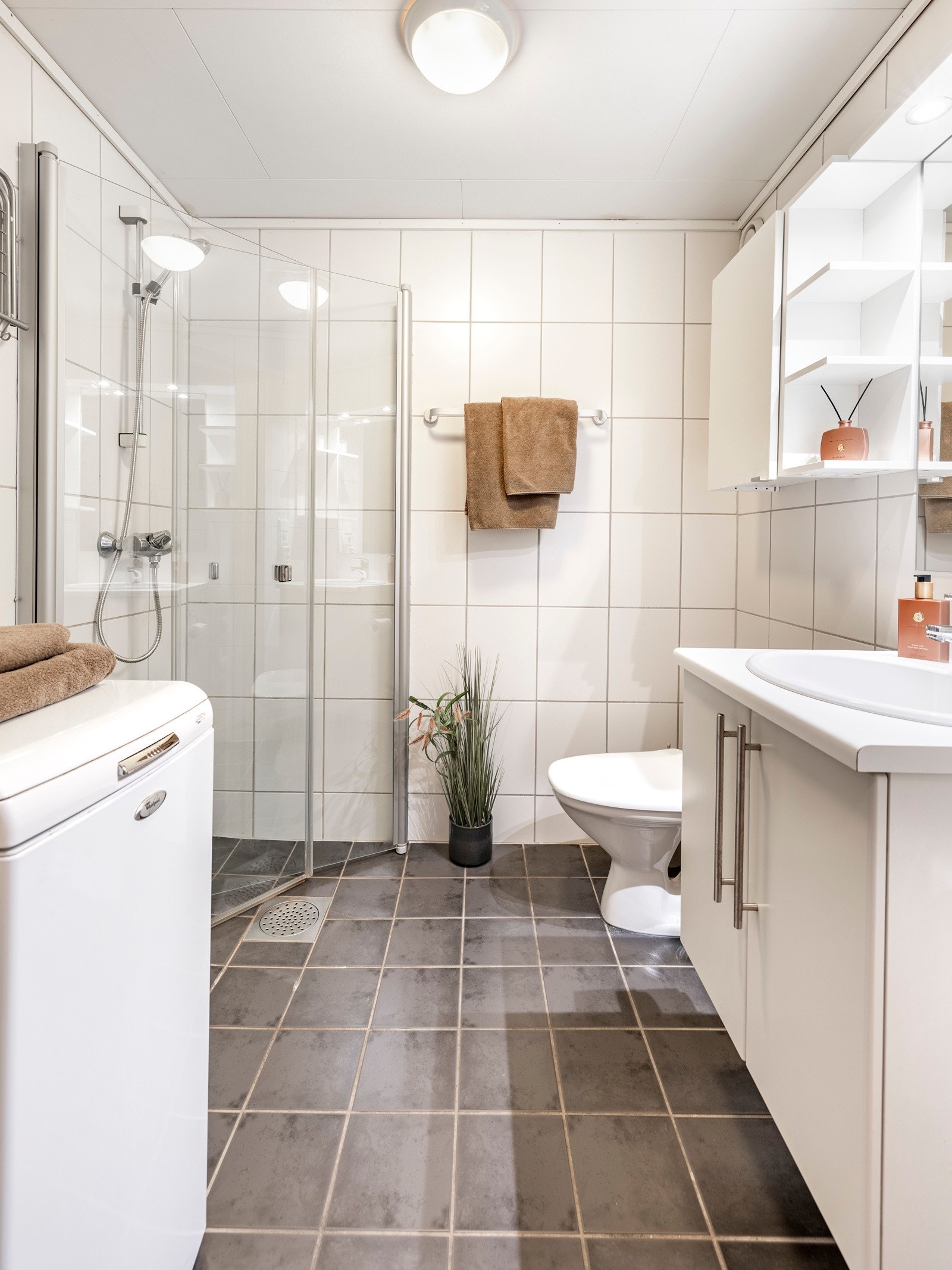 Badet er helfliset, har en fin størrelse og opplegg for vaskemaskin. Det er grå fliser på gulv med gulvvarme, hvite fliser på veggene, plafond i taket og mekanisk avtrekk. Galleribilde