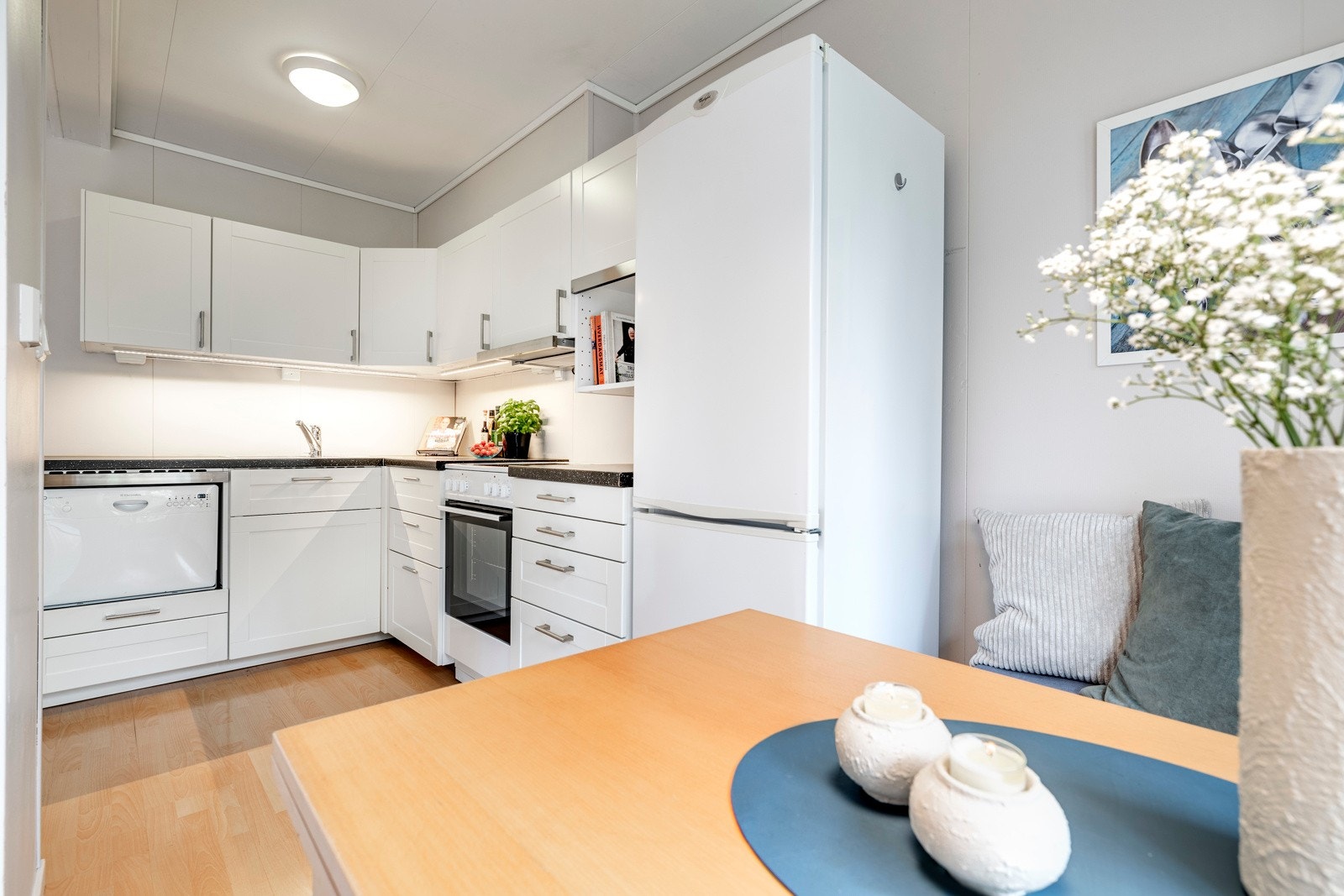 Kjøkkenet har en pen innredning fra Ikea plassert i L-form, åpent mot stuen. Innredningen er holdt i en klassisk stil med hvite, profilerte fronter og benkeplate i mørk laminat med nedfelt vaskekum i stål. Galleribilde