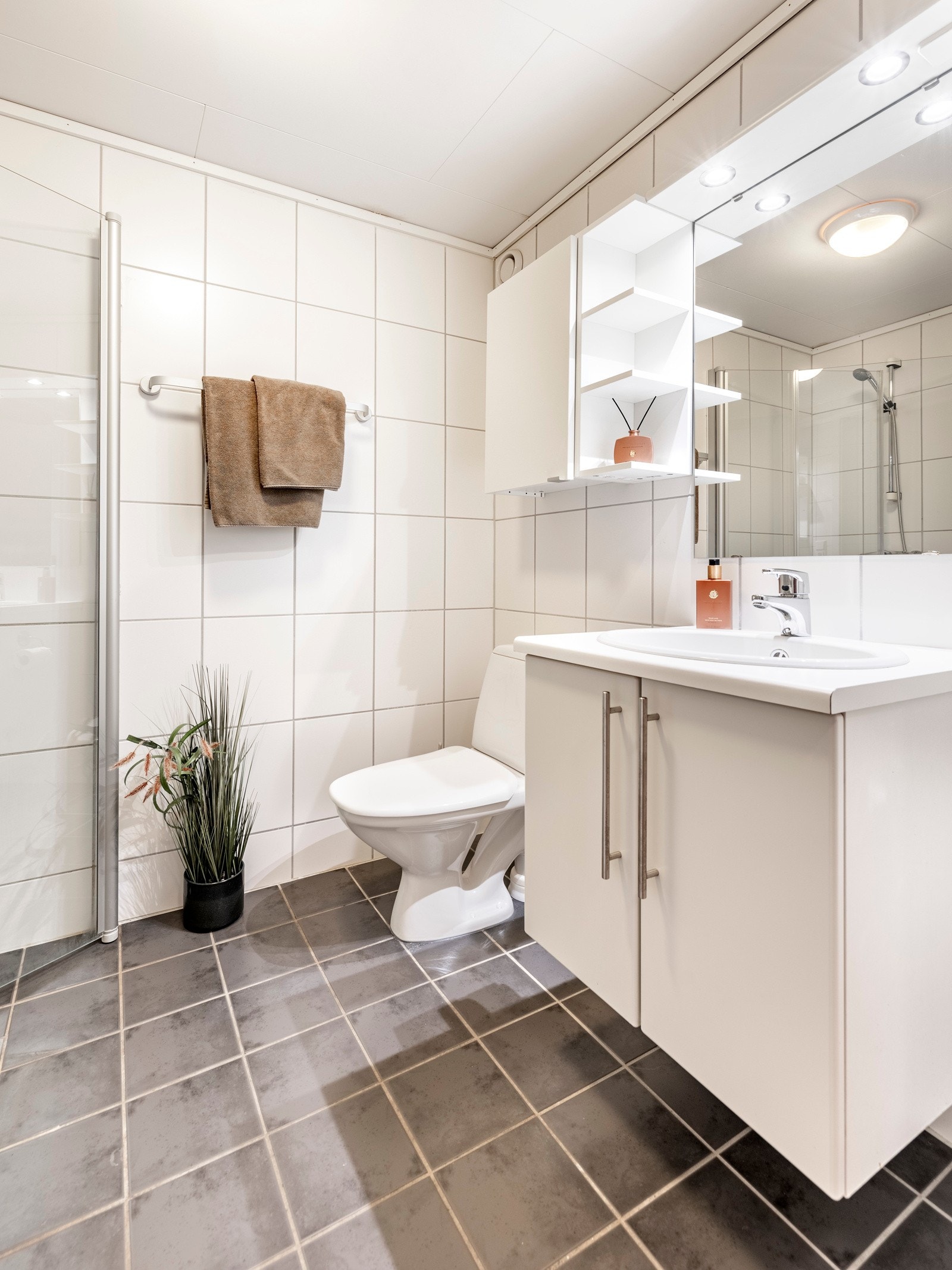 Badet er helfliset, har en fin størrelse og opplegg for vaskemaskin. Det er grå fliser på gulv med gulvvarme, hvite fliser på veggene, plafond i taket og mekanisk avtrekk. Galleribilde