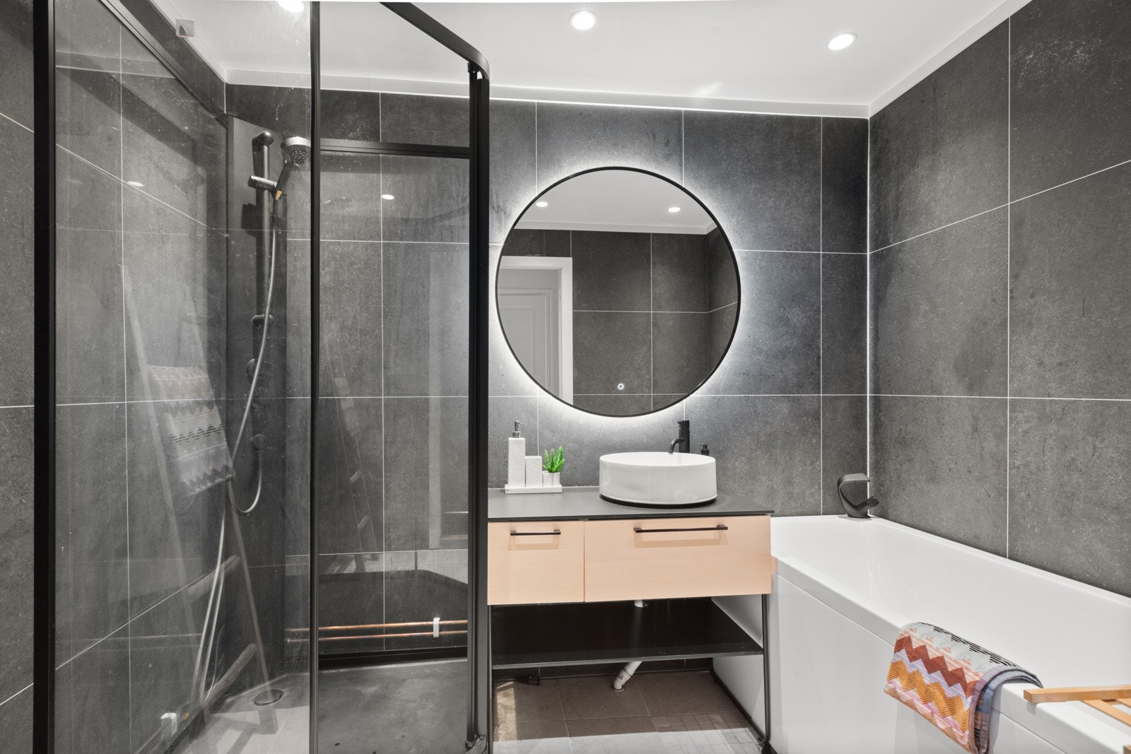 Pent baderom med både dusjkabinett og badekar og servantskap og designspeil med belysning Galleribilde