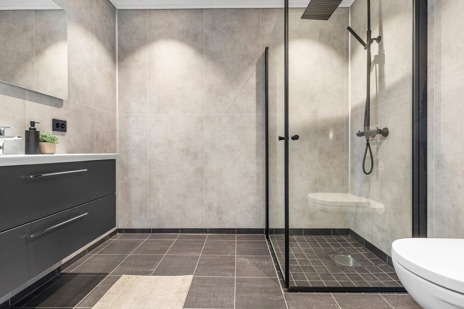 Mørke fliser på gulv, med lyse baderomsplater og sorte detaljer, gir badet et moderne uttrykk. Baderomsinnredning med praktiske skuffer for oppbevaring Galleribilde