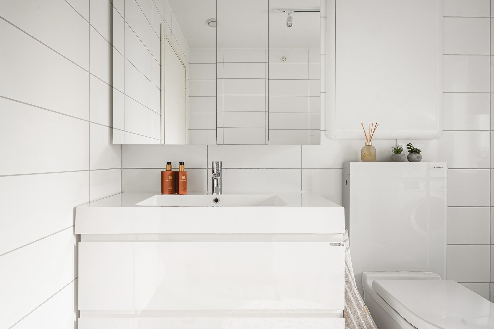 Moderne, lys baderomsinnredning med mye oppbevaringsplass samt overspeilskap.