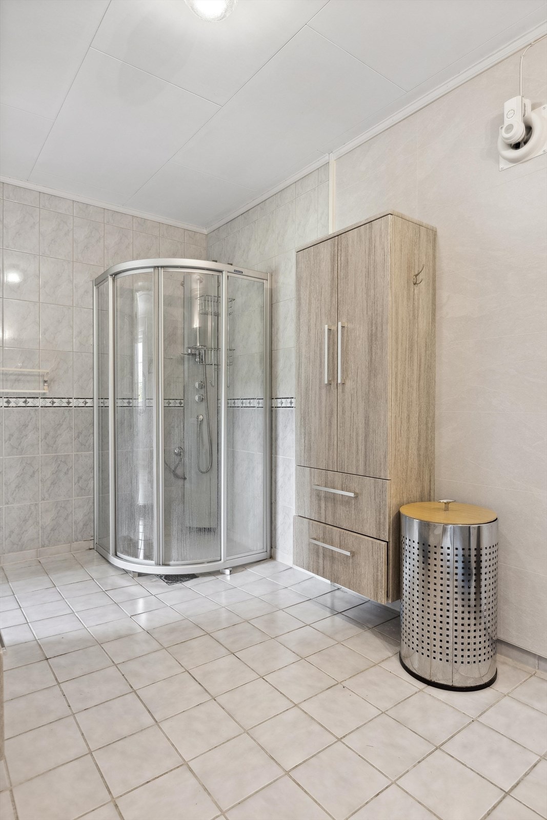 På overflater er det flislagt gulv med varmekabler, dels flislagt og dels baderomsplater på vegger samt folierte plater i himling. Av sanitær er det servant med skuffer, wc og dusjhjørne med skyvedør i glass. Galleribilde