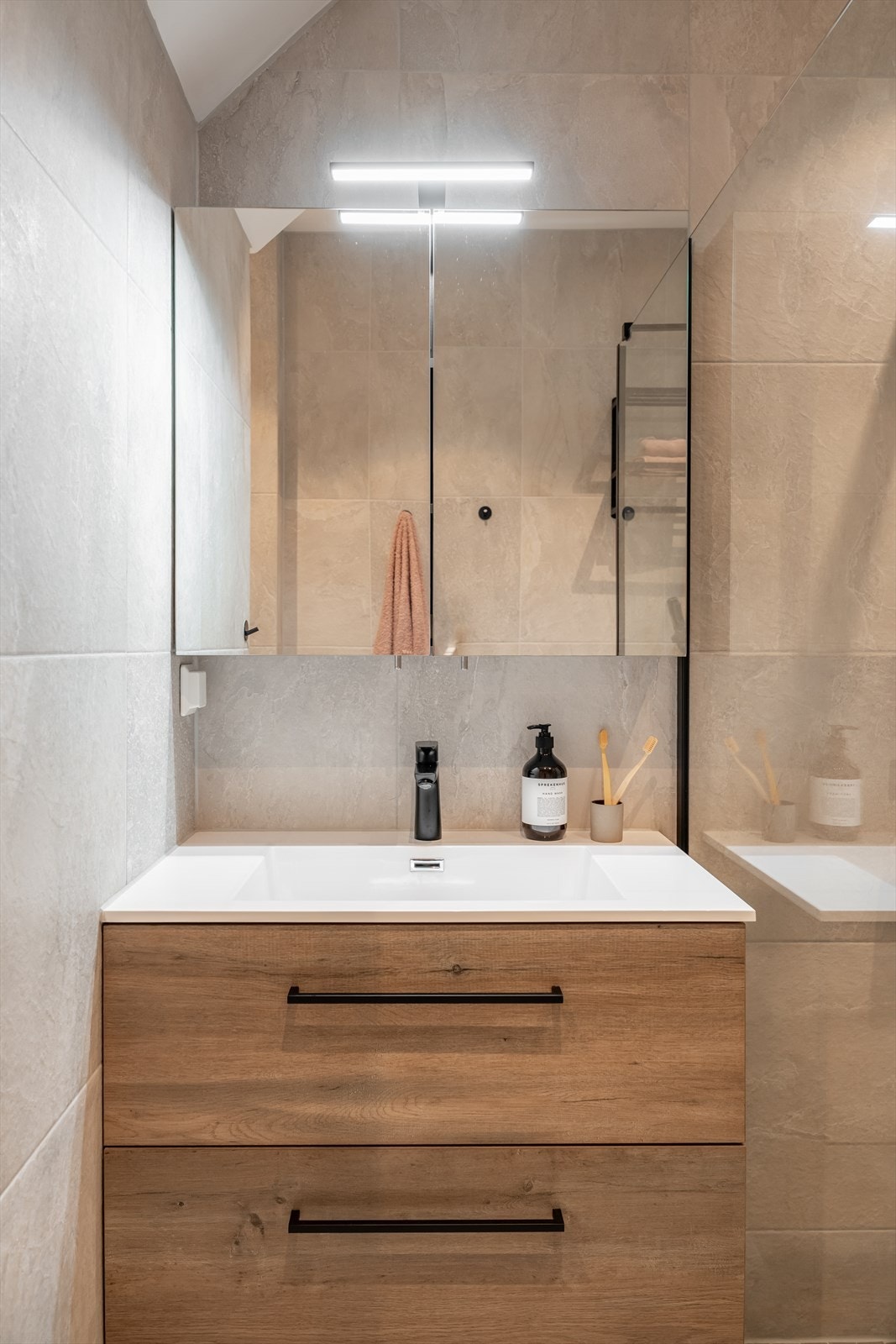 Badet er innredet med veggmonterte dusjvegger, veggmontert klosett, servant med skuffer, speilskap med belysning og opplegg for vaskemaskin. Galleribilde