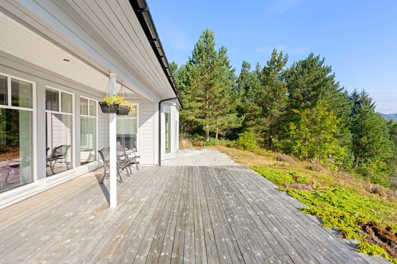 Langs boligens øst og sør-fasade er det en romslig markterrasse i trevirke Galleribilde