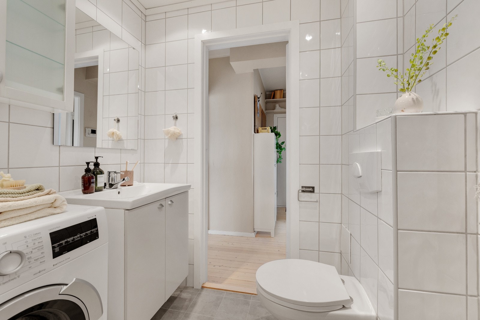 Badet inneholder vegghengt innredning med heldekkende servant, speil, vegghengt toalett og dusjnisje med glassdør. Galleribilde