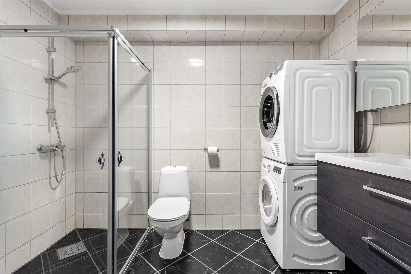 Romslig og innbydende flislagt bad med opplegg for vaskemaskin og tørketrommel. Galleribilde