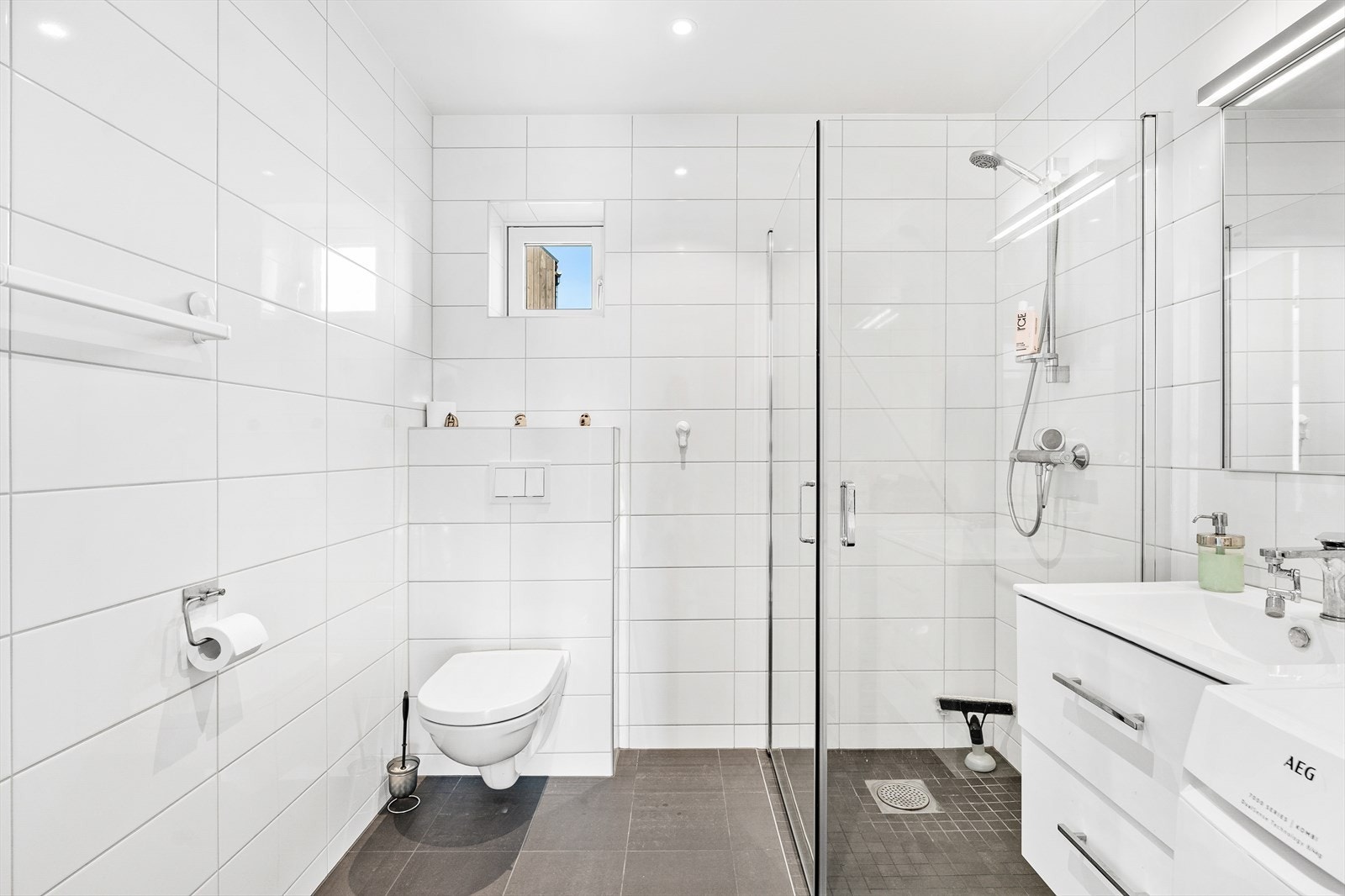 Ellers er badet utstyrt med vegghengt toalett, dusj, servant med belysning og opplegg for vaskemaskin. Galleribilde