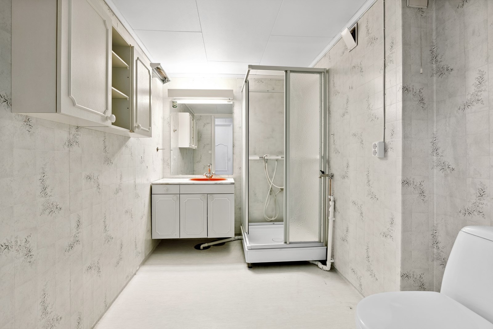 Badet er utstyrt med vinylbelegg på gulv, våtromstapet på vegger, innredning, toalett og dusjkabinett. Galleribilde