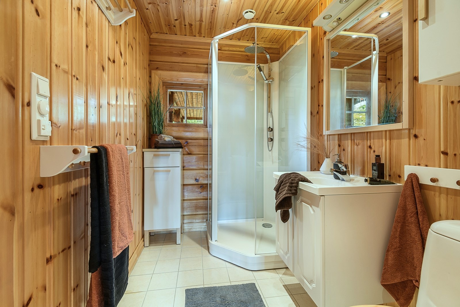 Bad med panelte vegger og fliser på gulv. Dusjkabinett, servantinnredning og gulvmontert WC. Galleribilde