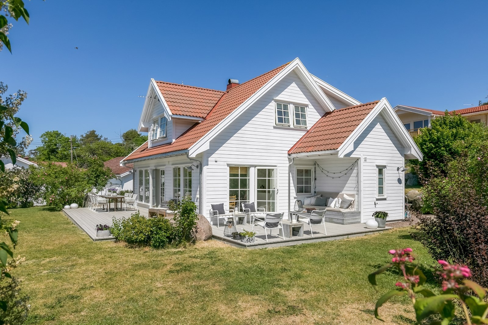 Pent opparbeidet hage med gressplen, prydbusker og stor markterrasse. Galleribilde