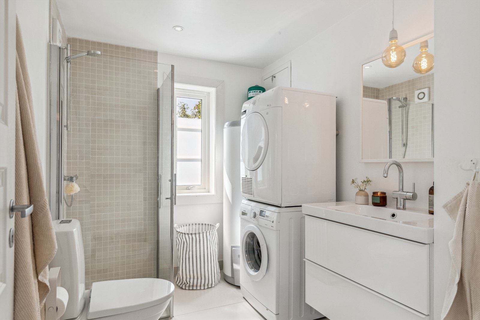 Lyst og pent bad med tusj, toalett, servant med underskap, og opplegg for vaskemaskin og tørketrommel. Galleribilde