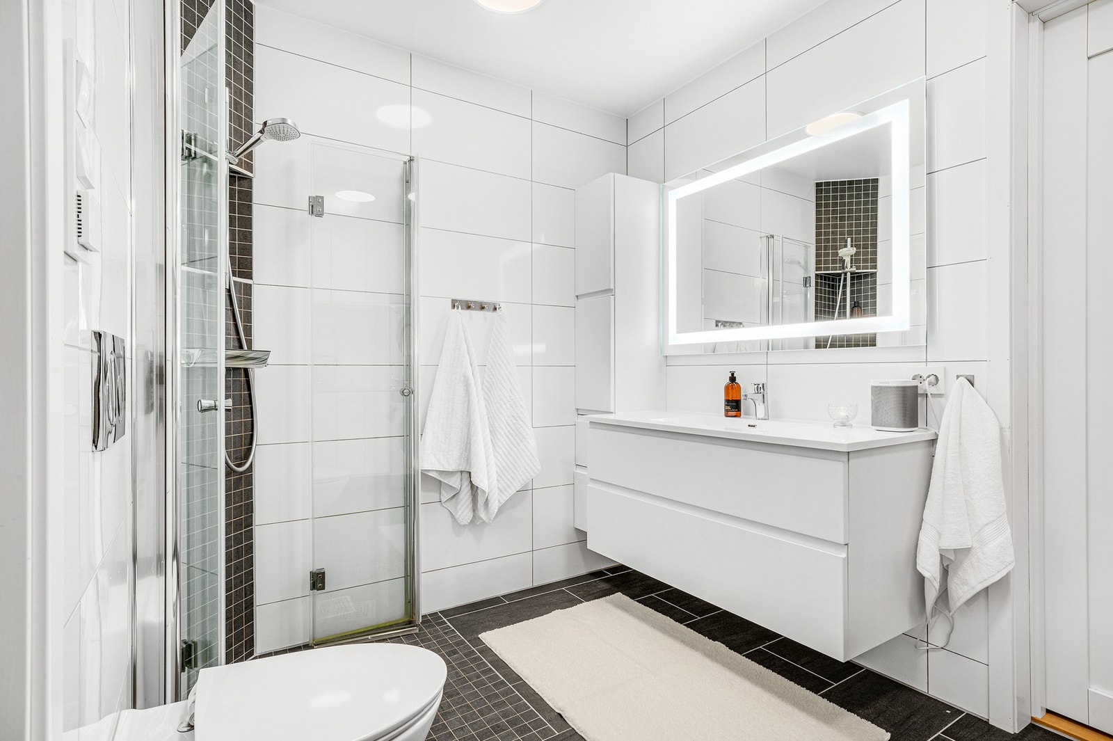 Delikat flislagt bad med hvit stilren innredning, toalett og stilig dusjhjørne. Galleribilde