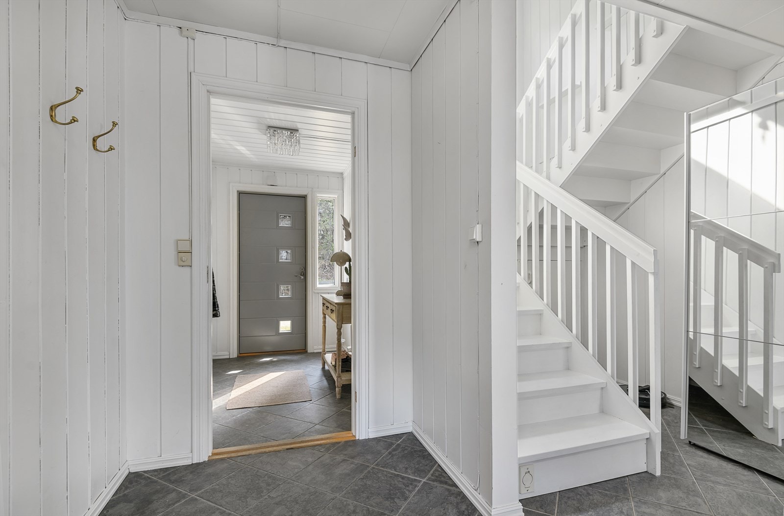 Hall/trapperom i 1. etg. er innredet med skyvedørsgarderobe med speilfronter. Malt tretrapp med tette trinn og oppbevaringsplass under trappen. Galleribilde