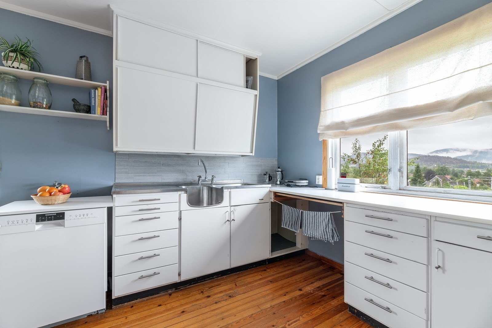 Romslig kjøkken med eldre innredning med hvitmalte, slette fronter på over- og underskap og skuffer. Galleribilde