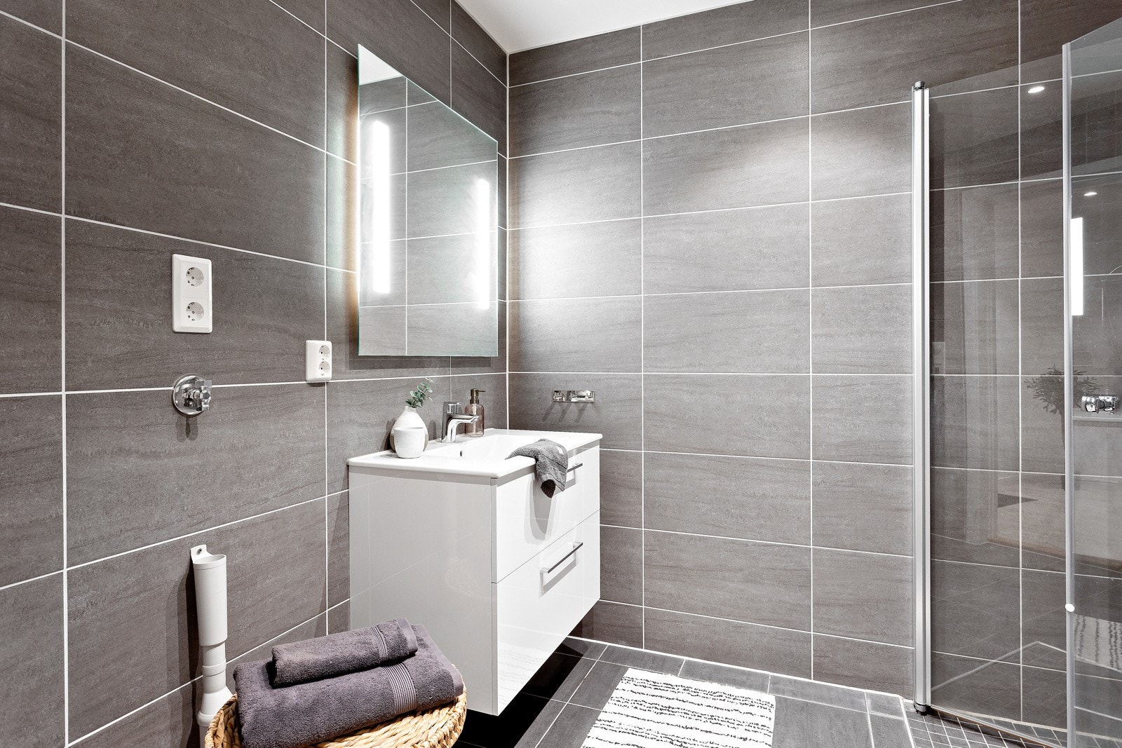 Badet er flislagt og pent. Her er det montert innredning med servant, lysspeil, vegghengt wc og dusjhjørne. Galleribilde