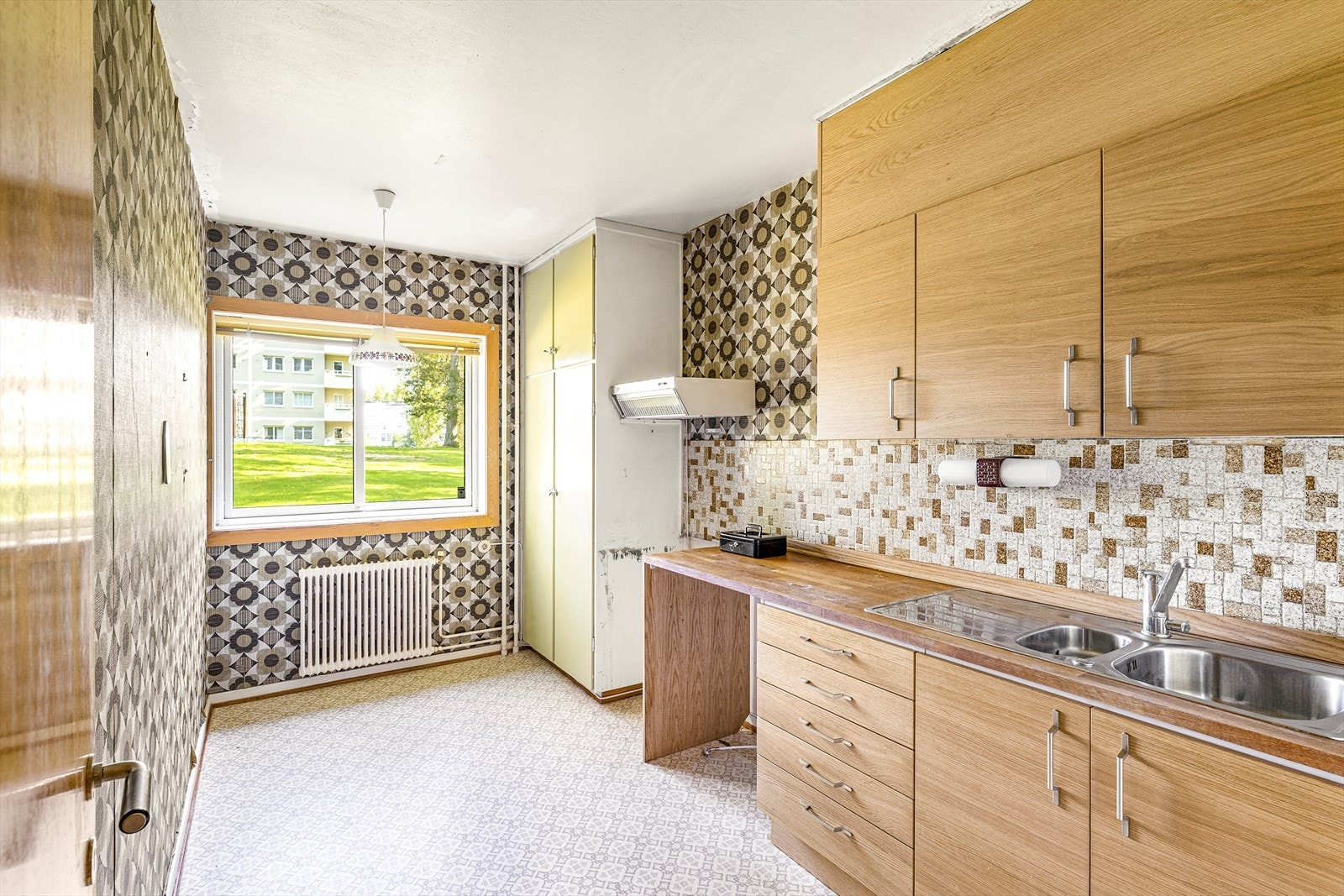 Eldre kjøkkeninnredning med belegg på gulv, tapet på vegger og malt tak. Galleribilde