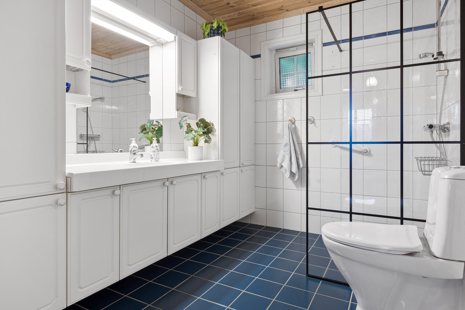 Badet er fra byggeåret og har blått flislagt gulv med behagelig gulvvarme og lyse flislagte veggoverflater Galleribilde