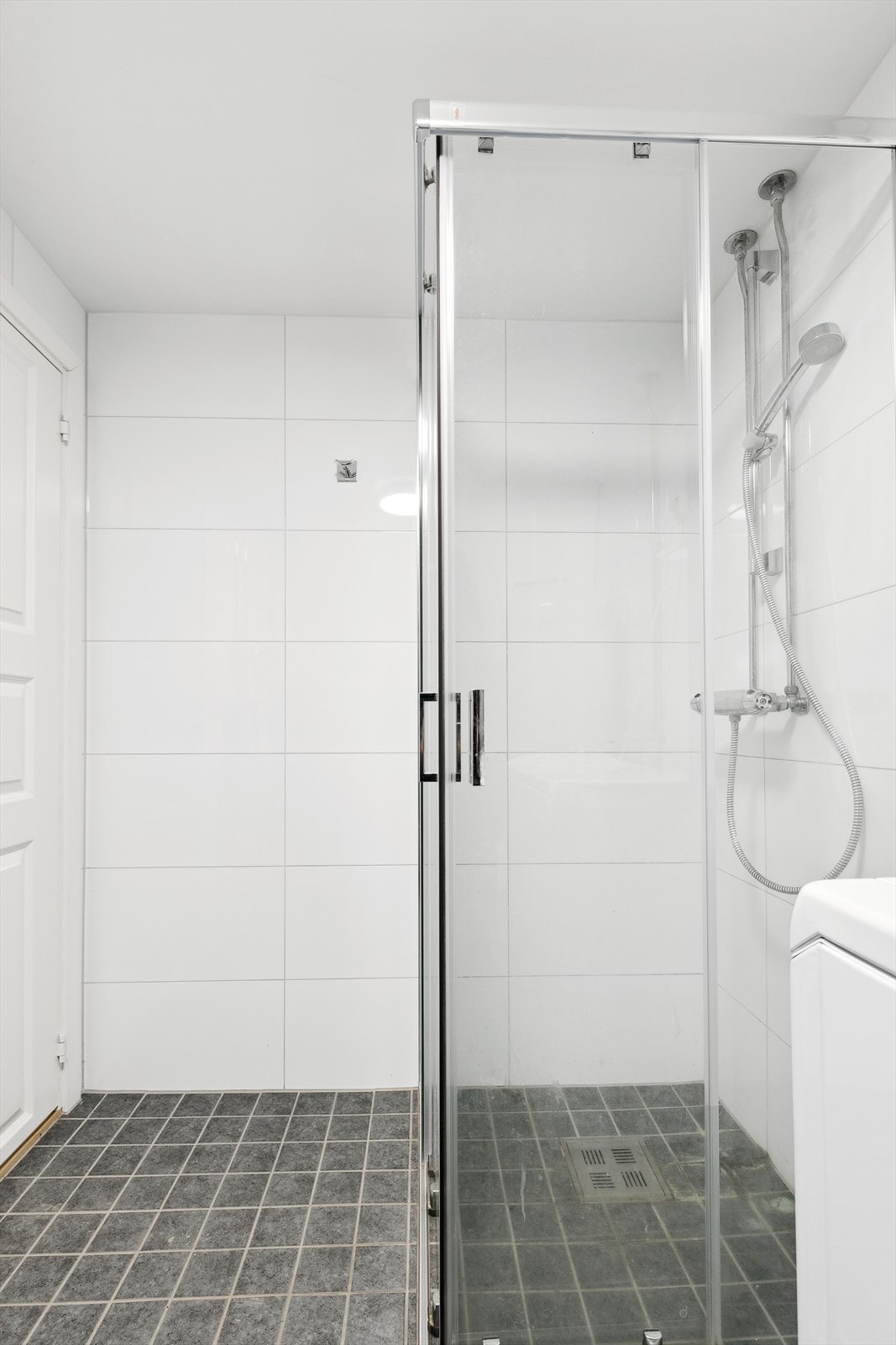 Badet er utstyr med dusjhjørnet med gulvskinne, skyvedører i glass og ettgreps dusjbatteri i rustfritt stål og skyllekum. Galleribilde