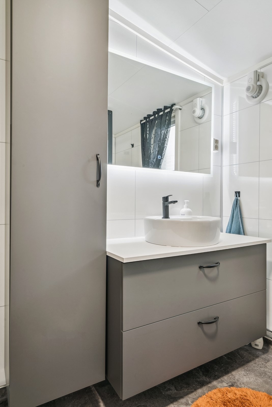 Badet er innredet med en tøff, moderne innredning med servant, underskap med uttrekkbare skuffer og et høgskap, stort vegghengt speil med innebygget belysning, dusjkabinett og gulvmontert toalett Galleribilde